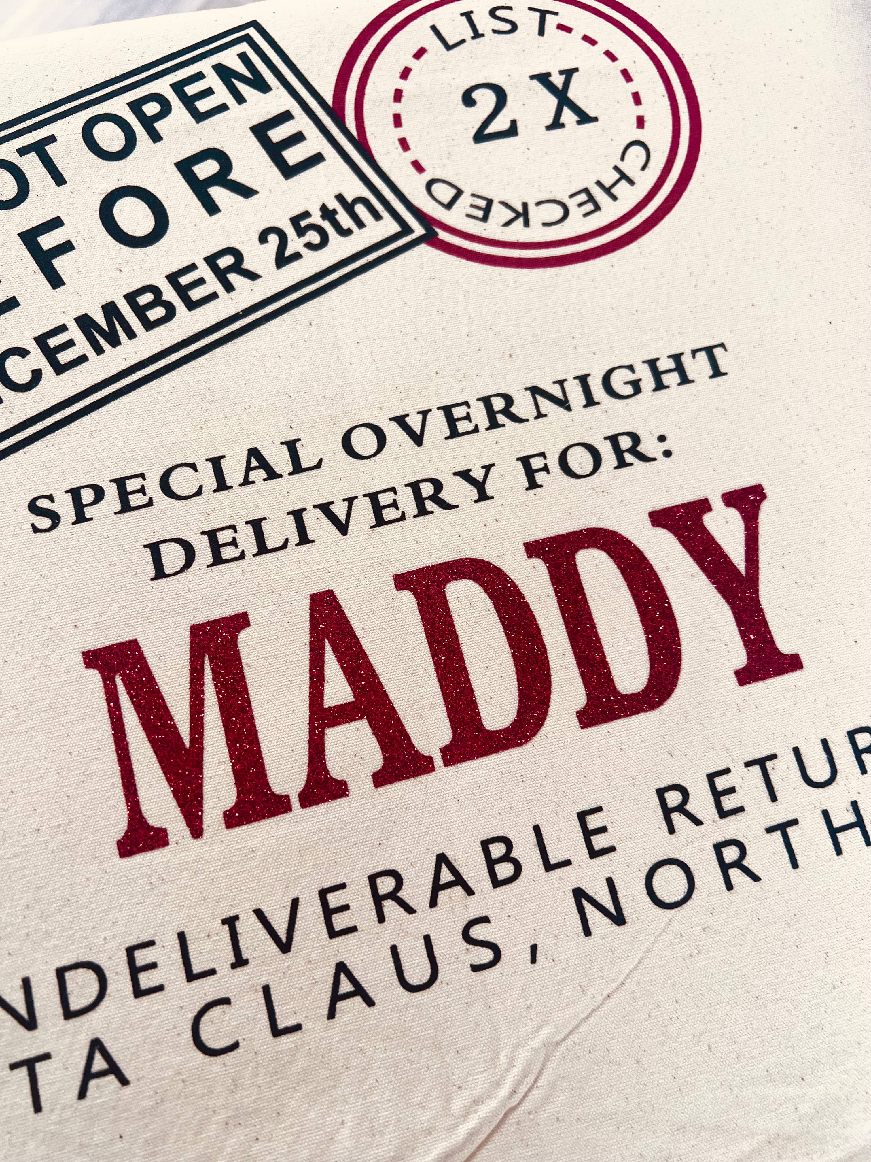 personalised santa sack with text 'Special overnight delivery for MADDY' and 'Not open before December 25th' on a textured background.